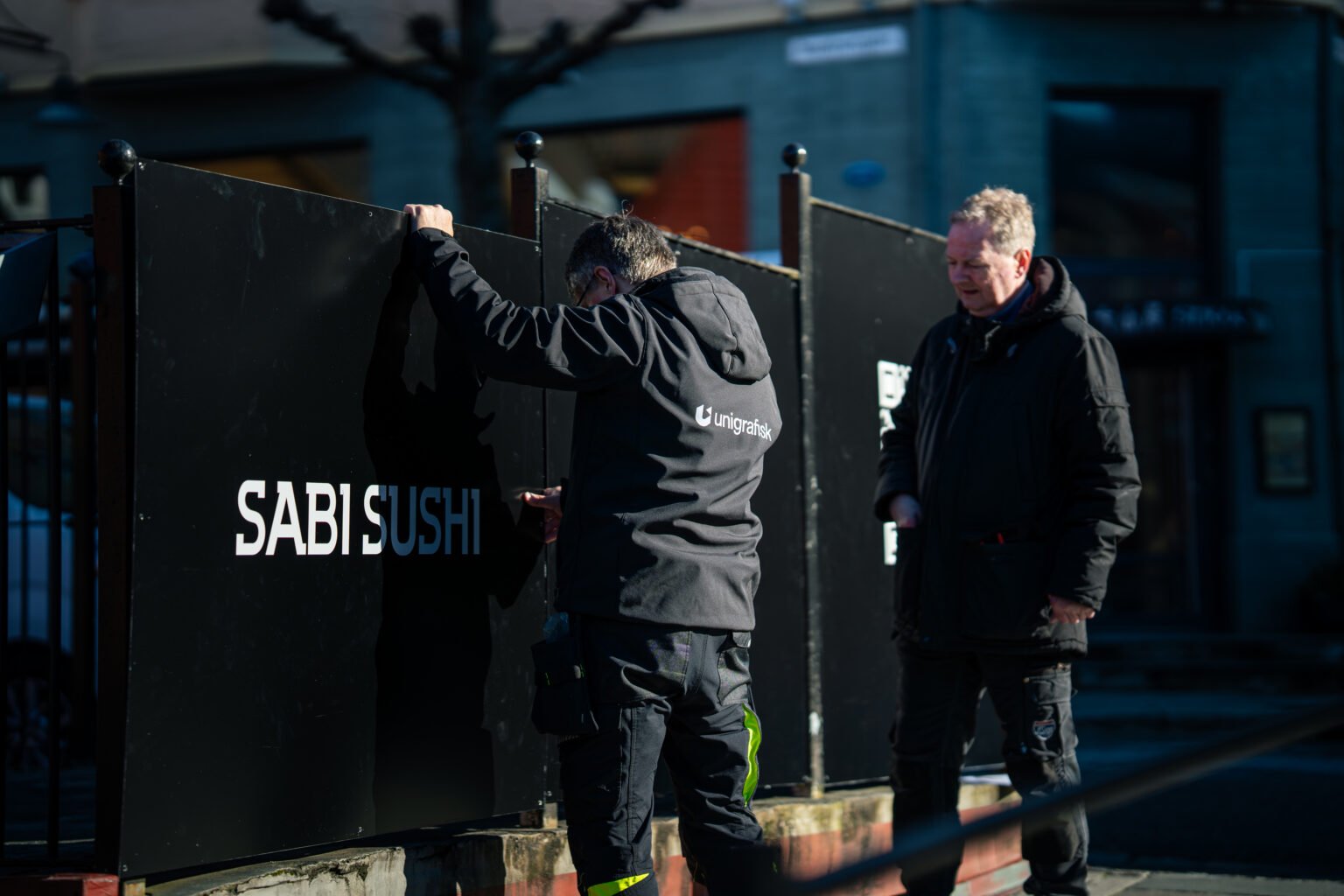 To montører fester et Sabi Sushi-skilt i Bergen sentrum