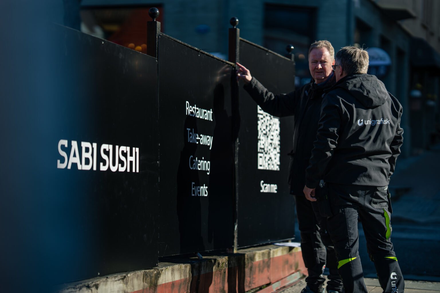 Montører fester Sabi Sushi-skilt på gjerdet ved uteserveringen
