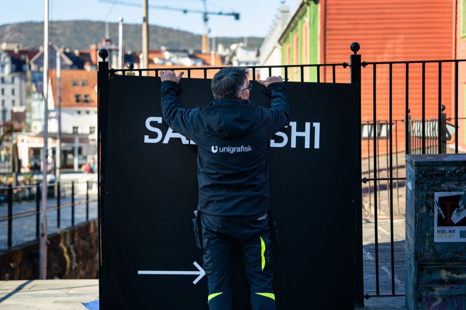 Montør fester et Sabi Sushi-skilt på gjerdet med utsikt over Bergen